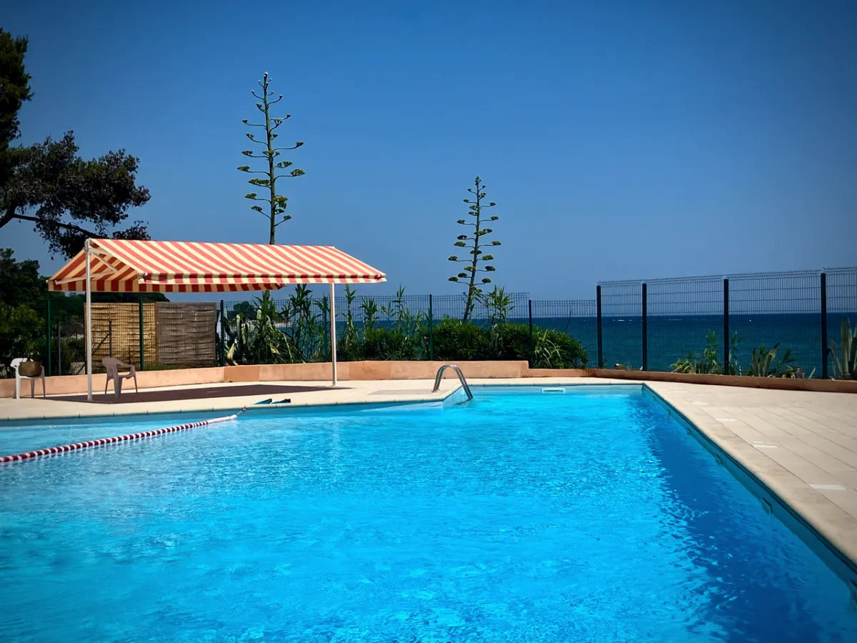 Grande piscine bleue, auvent rayé et horizon mer au fond