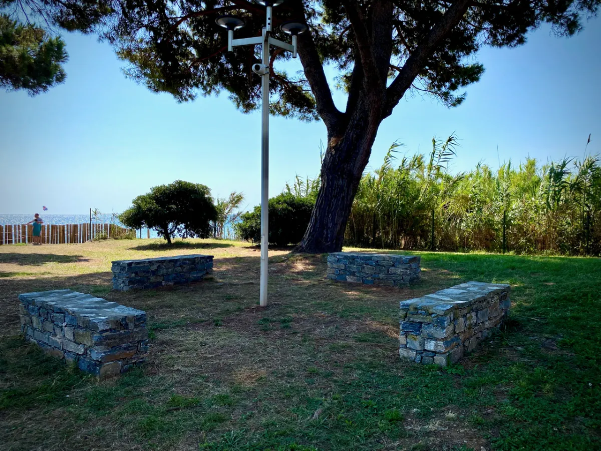 Espace détente avec bancs en pierre sous les arbres, près de la plage